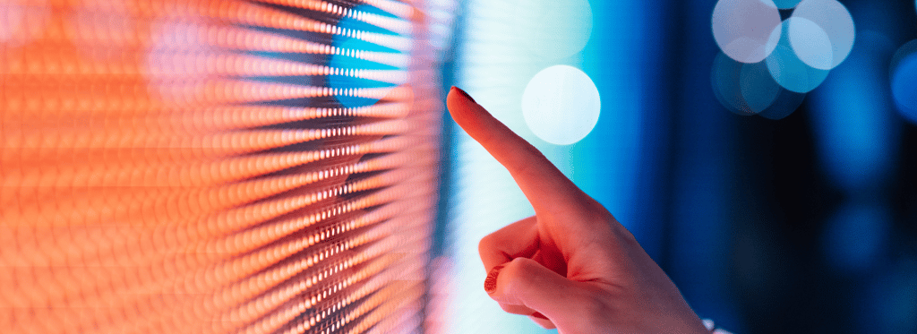 Hand pointing at a colourful LED screen with orange and blue pixels.