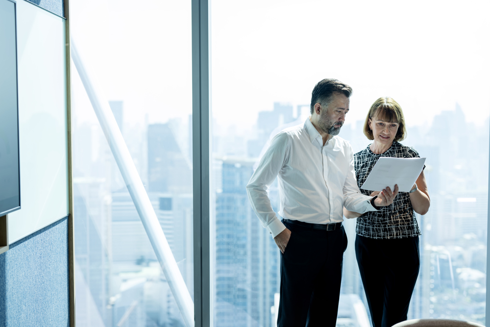 A man and a woman reviewing an environmental audit report, standing near the office window